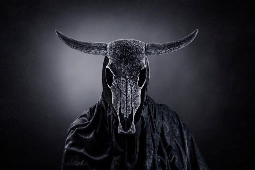 Figura espeluznante con cráneo de animal con cuernos en la oscuridad photo