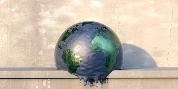 A spherical model of planet earth sitting on a concrete shelf on a hot day, deflating and melting. The globe has a blue 'sea' and metallic green 'land' and has drips forming at it's base as it heats up. Plenty of copy space.