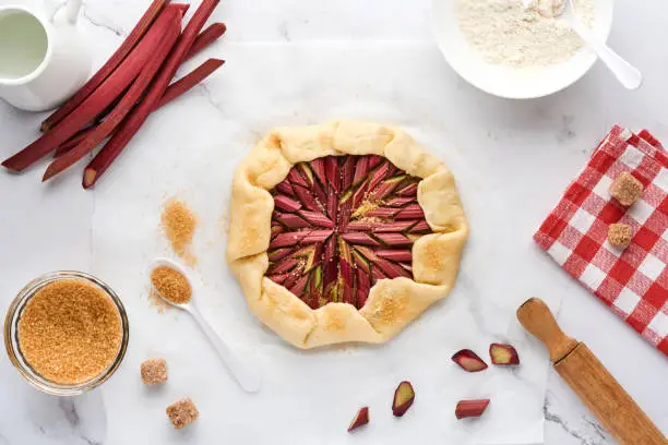 Galette with fresh rhubarb process of preparation and ingredients flour, water, butter, sugar and rhubarb for baking on white marble background. Christmas and New Years baked goods. Top view.