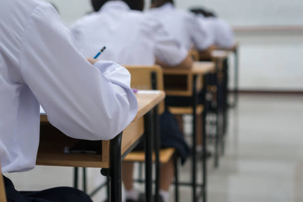 Writing test in exam with behind girl Asian students group concentrate in high school, serious taking final examination desk at classroom with Thai student uniform. Education evaluation back to school stock photo