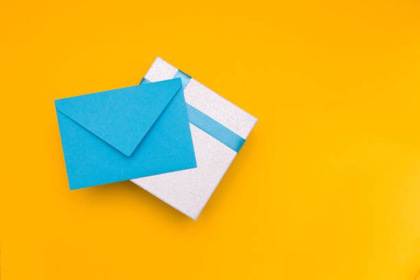 istock blue envelope lies on a silver shiny box with a blue ribbon, yellow background, copy space, top view 1317977699