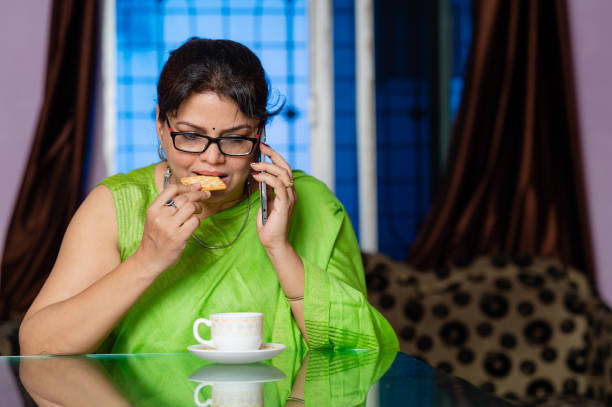 istock Adult women using smartphone , drinking tea with biscuit while sitting on sofa at home. 1317978975