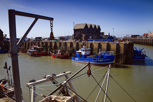 Whitstable Harbour, Kent, England, UK - April 2021. Fishing boats moored at Whitstable harbour are part of a fleet that catches shellfish in the local bay. Warehouses and machinery for processing the catch can be see around the quay.