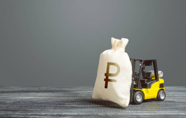 Yellow forklift carries a russian ruble money bag. Big contract, profitable deposit, take a loan. Inflation, price increases. Wealth, investments in economy. Grants financing. Payment of taxes. la carretilla elevadora amarilla lleva una bolsa de dinero de rublo ruso. gran contrato, depósito rentable, tomar un préstamo. inflación, aumentos de precios. riqueza, inversiones en economía. financiación de subvenciones. pago de impuestos.