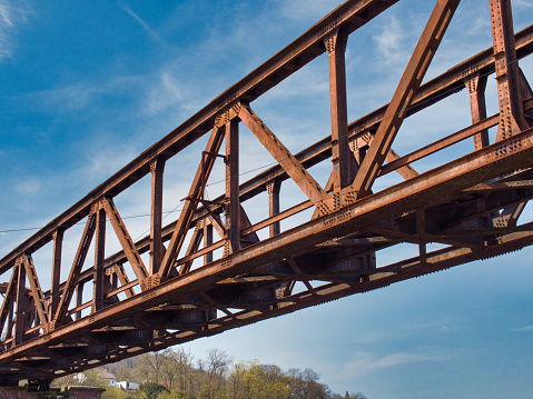 A rusty metal truss bridge under a sunny blue sky full of clouds