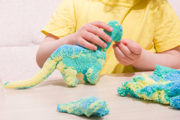 istock the child plays plasticine from polymer granules at the table, the original plasticine from tiny balls, the child plays with a dinosaur from plasticine, what to play with the child at home 1317984576