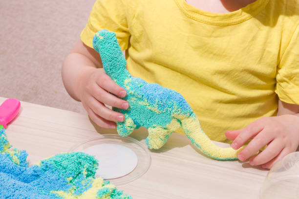 istock the child plays plasticine from polymer granules at the table, the original plasticine from tiny balls, the child plays with a dinosaur from plasticine, what to play with the child at home 1317984577