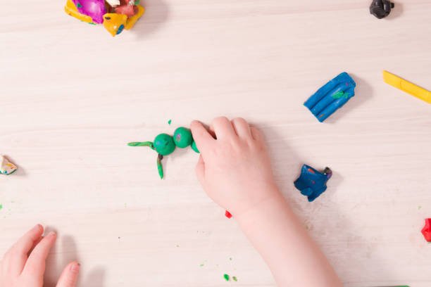 istock a small child sculpts a caterpillar from green plasticine on a wooden table, the development of fine motor skills of hands than to entertain a child at home, stay at home 1317984797