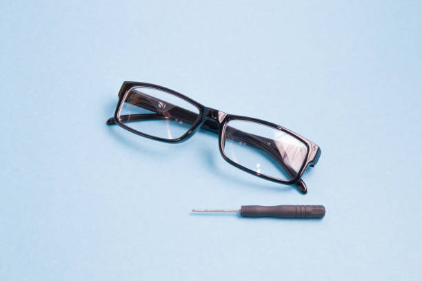 istock glasses in a black plastic frame and a small screwdriver are on a light blue background, broken glasses are under repair 1317985737