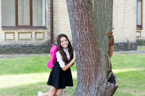 istock Happy little kid in school uniform with backpack observe squirrel climbing tree in park, outdoor education 1317987541