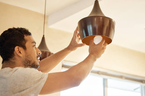 cropped shot of a young man replacing a light bulb at home - energy saving fotos imagens e fotografias de stock