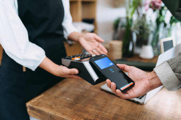 fermez-vous vers le haut du magasin de jeune homme asiatique au magasin de fleur. il paie avec son smartphone, scanne et paie une facture sur une machine à cartes effectuant un paiement rapide et facile sans contact. technologie nfc, concept tap and go - point de vente photos et images de collection