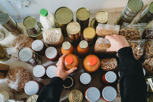 Woman is rearranging the nonperishable food at the food bank. Many cans, bottles and tins on the kitchen table.