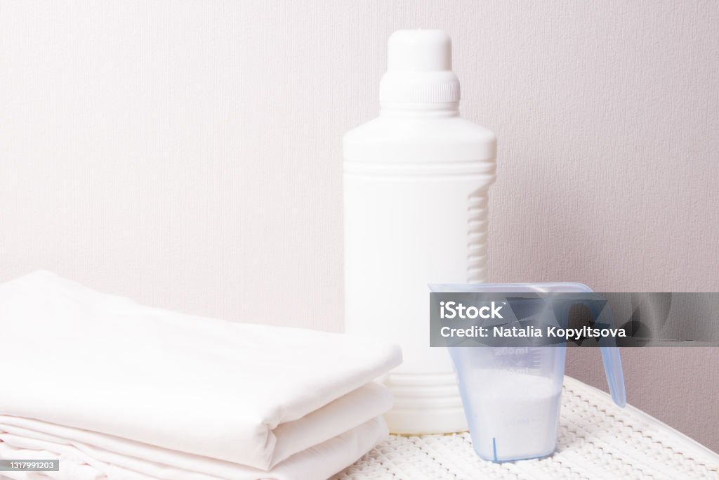 White Plastic Bottle With Bleach And Laundry Detergent In A Measuring Cup  On A White Plastic Basket For Dirty Laundry Light Background Copy Space Wash  White Linen Concept Stock Photo - Download