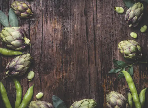 Rustic, wooden, food cooking and healthy eating springtime background, internet banner with fresh Broad bean or  fava beans (Fave) and artichokes. From garden to table: springtime vegetables