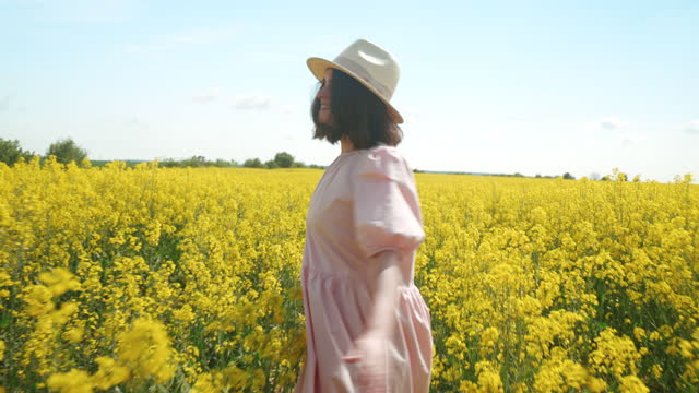 Happy young woman enjoying beautiful moments in nature. She is looking at camera while running through a oilseed rape field. Slow motion scene.