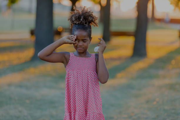 Allergic Cute Little Girl with Curly Hair is Rubbing her Eyes in the Park. Beautiful African-American Girl with Sight or Allergy Problems is Rubbing her Eyes During the Walk in a City Park on Sunny Day. human eye scratching allergy rubbing stock pictures, royalty-free photos & images