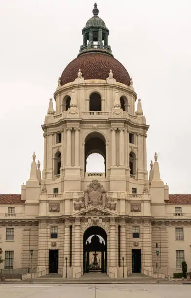 Pasadena, CA, USA - May 11, 2021: Closeup of Beige stone, look-through, sculpted tower with red tiled dome and greenish top of historic City Hall under silver sky.