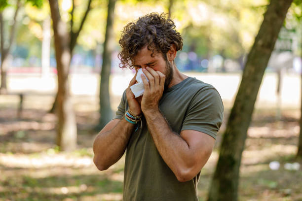 Man With Seasonal Flu is Walking in Park and Coughing in Paper Tissues. Sick Man With High Temperature is Using Handkerchiefs, Trying to Override the Sickness While Walking in Nature. cold and flu man stock pictures, royalty-free photos & images