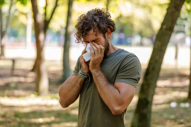 Photo of Man With Seasonal Flu is Walking in Park and Coughing in Paper Tissues.