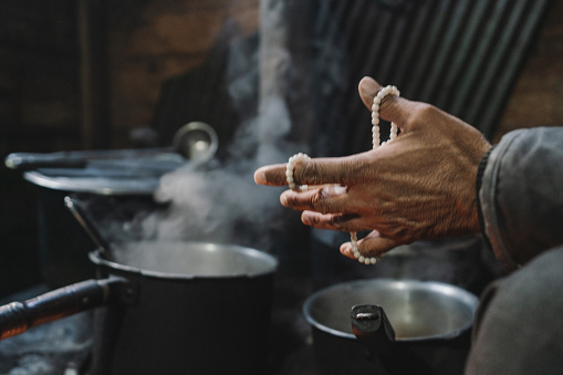 Close up of man's hands with prayer beads above the steaming pots