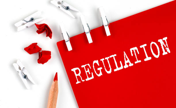 istock REGULATION text on red paper with office tools on white background 1317997056