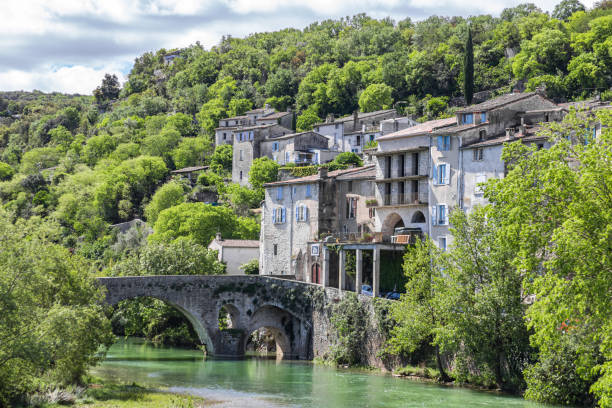 View of the old houses and the forest of the medieval village of Sauve from the banks of the Vidourle (Occitanie, France) stock photo