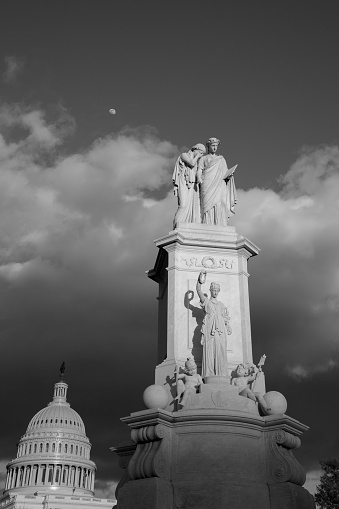 Peace Monument at sunset with storm clouds gathering and the moon in the background behind the United States Capitol. Also known as the Naval Monument or Civil War Sailors Monument.