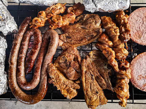 Braaied meat on a grid including Boerewors, lamb chops, chicken kebabs, beef burgers and garlic rolls