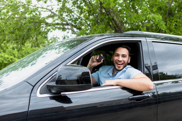 Man holds up keys and smiles after online car purchase The mid adult man holds up the keys to his new car and smiles.  He has just purchased his car online. car rental covid stock pictures, royalty-free photos & images