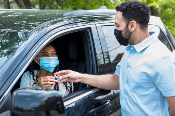 Woman receives keys for new car from salesman Sitting in her new car, the mid adult woman receives the keys for the car from the mid adult salesman.  They both wear masks because of COVID-19. car rental covid stock pictures, royalty-free photos & images