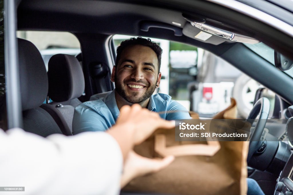 Man smiles while picking up curbside order The mid adult man smiles when his curbside order is handed to him through the passenger window of his car. Curbside Pickup Stock Photo