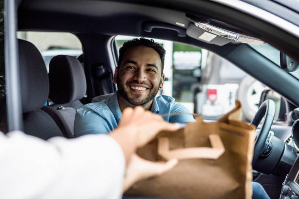 Man smiles while picking up curbside order The mid adult man smiles when his curbside order is handed to him through the passenger window of his car. food delivery stock pictures, royalty-free photos & images