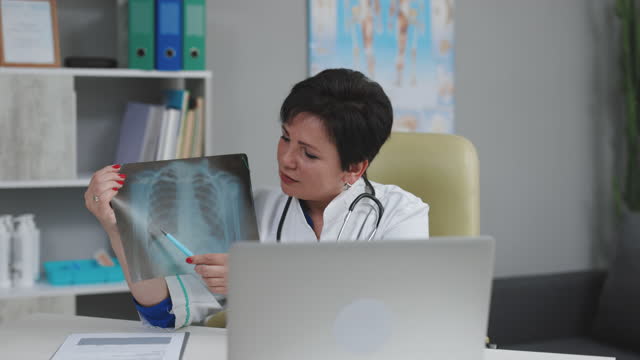 Professional female doctor in white medical coat making conference call on laptop computer, consulting distance patient online in video chat, explain treatment by webcam concept