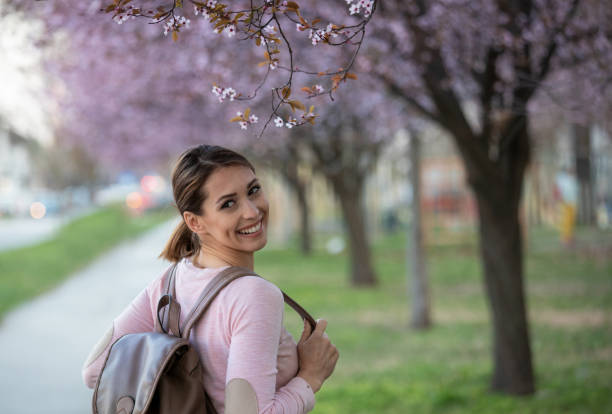 istock Girl with backpack on shoulder walking on street with blooming tree 1318007937