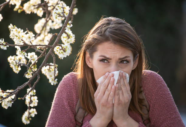 istock Woman sneezing in front of blooming tree 1318007980