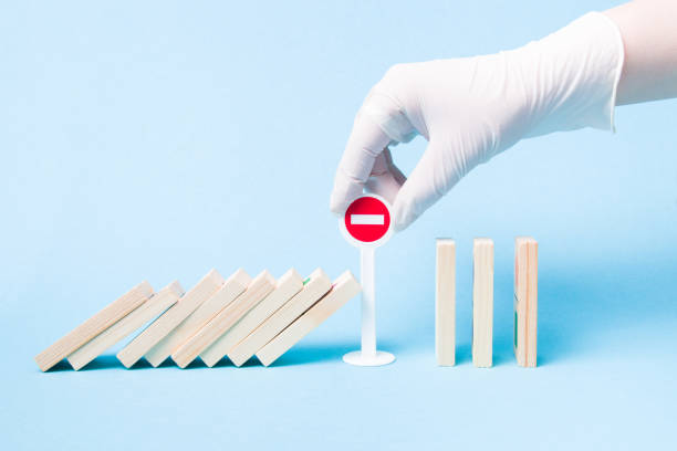 istock hand in a white medical rubber glove stops a domino from falling using a plastic toy miniature stop sign, blue background, self-isolation and quarantine concept, stop a pandemic, stay home 1318010151