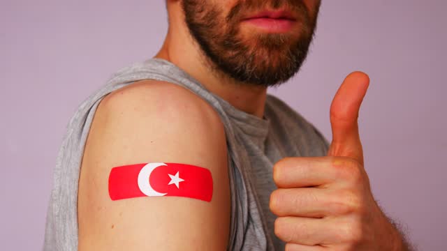 Close-up of a man showing the Turkey flag bandage on his right arm after COVID-19 vaccination and raised thumb of the other hand