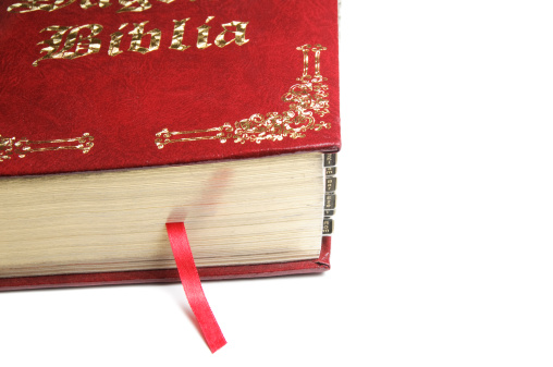 A red Spanish Bible with decorative gold trim and lettering and a red ribbon page marker.