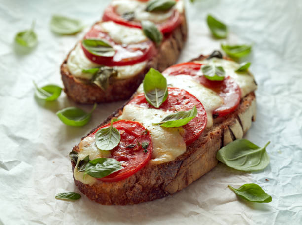 Grilled caprese sandwich based on sourdough bread with the addition of tomatoes, mozzarella cheese, fresh basil and olive oil on a light background Grilled caprese sandwich based on sourdough bread with the addition of tomatoes, mozzarella cheese, fresh basil and olive oil on a light background close-up crostini stock pictures, royalty-free photos & images