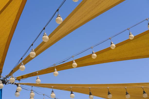 dynamische textur des stoff-stretchdachs aus segeltuch mit reihen von glühbirnenlampen für party-nachtbeleuchtung auf blauem himmelshintergrund. - shade sail awning textile stock-fotos und bilder