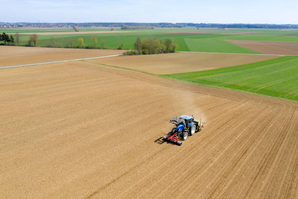 Tractor sowing and cultivating field in spring Aerial view of a blue, modern, agricultural tractor cultivating and sowing field in spring. overcasting stock pictures, royalty-free photos & images