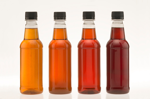 4 bottles of honey of different colors, on a white background.