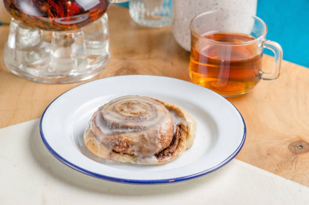 Vegan swedish cinnamon buns rolls with topping. Cinnabon in plate with tea cup on table. pasteles de ideas y recetas - rollos de canela perfectos con cobertura. bollos de canela sueco vegano kanelbullar con especias de calabaza, ingredientes de queso crema vegano en plato con taza de té en la mesa. plano laico o vista superior