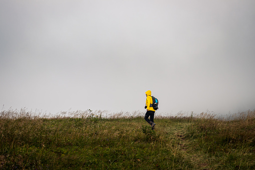 Tourist walking at meadow in wind and bad weather. Woman wearing waterproof sports clothing