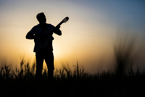Silhouette of Male musician playing acoustic guitar on sunset background