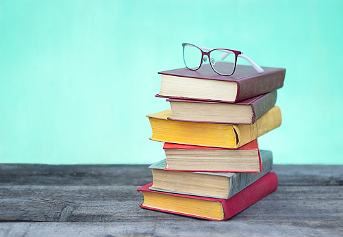 Glasses and a stack of six multi-colored books lie on a wooden table