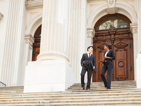 A well dressed man and woman in discussion as they as they walk down steps of a courthouse  building. Could be business or legal professionals.