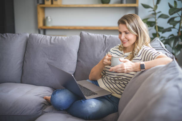 istock attractive middle aged woman sitting on the couch( laptop) 1318022804