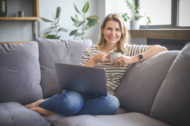 istock attractive middle aged woman sitting on the couch( laptop) 1318024887